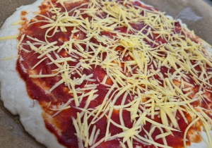 Bezglutenowa pizza przygotowana w kilku wariantach dietetycznych. Na blasze kawałki pizzy z sosem pomidorowym i startym serem.